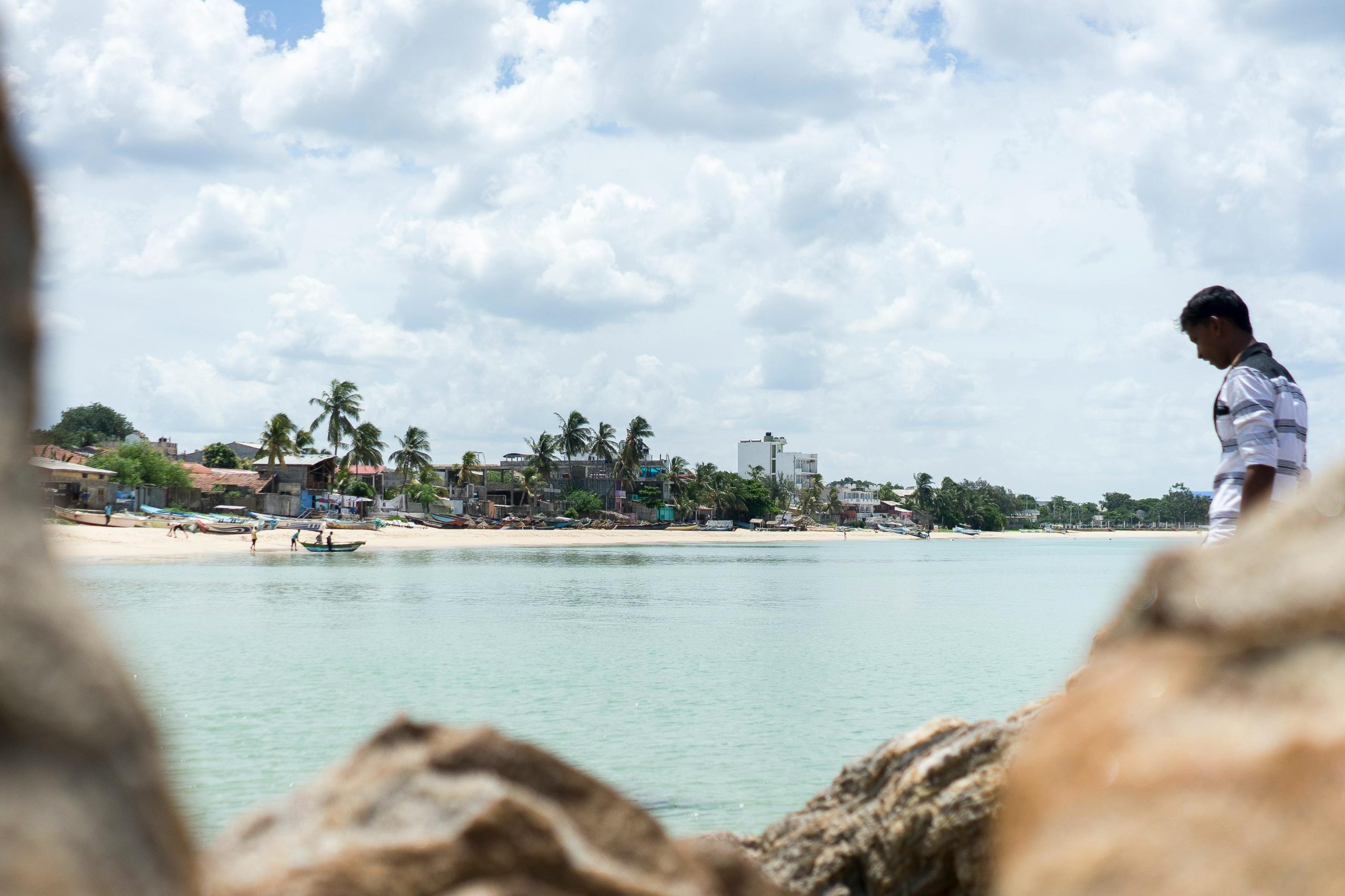 Scenic view of a Trincomalee beach with palm trees and a man in the foreground.