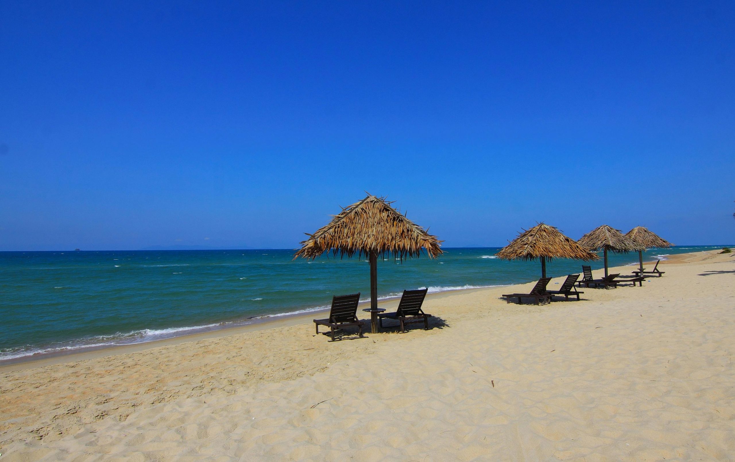Peaceful sandy beach with thatched umbrellas and clear blue sea under a sunny sky.