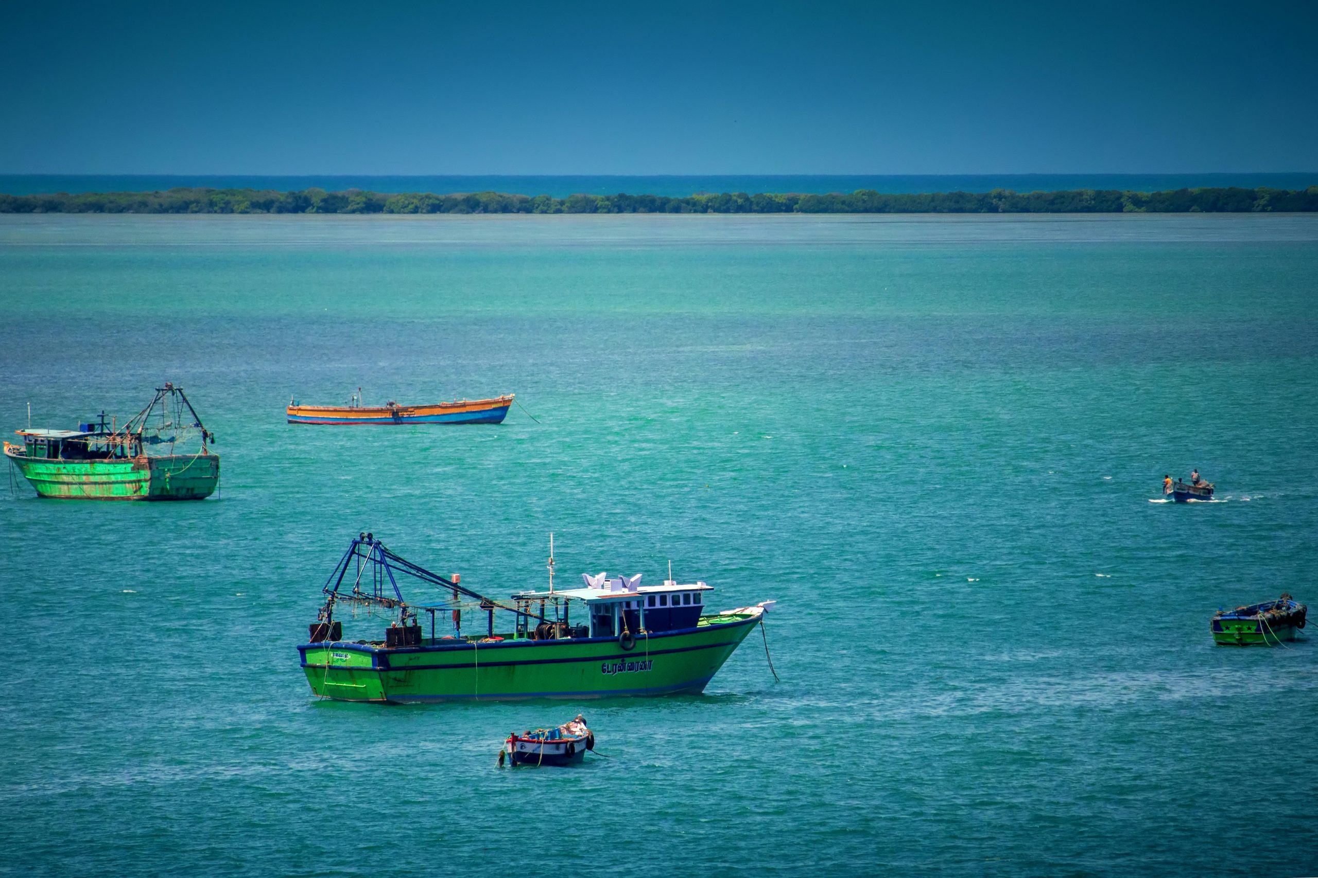 A scenic view of fishing boats on the turquoise sea near Dhanushkodi, India, under a clear summer sky.