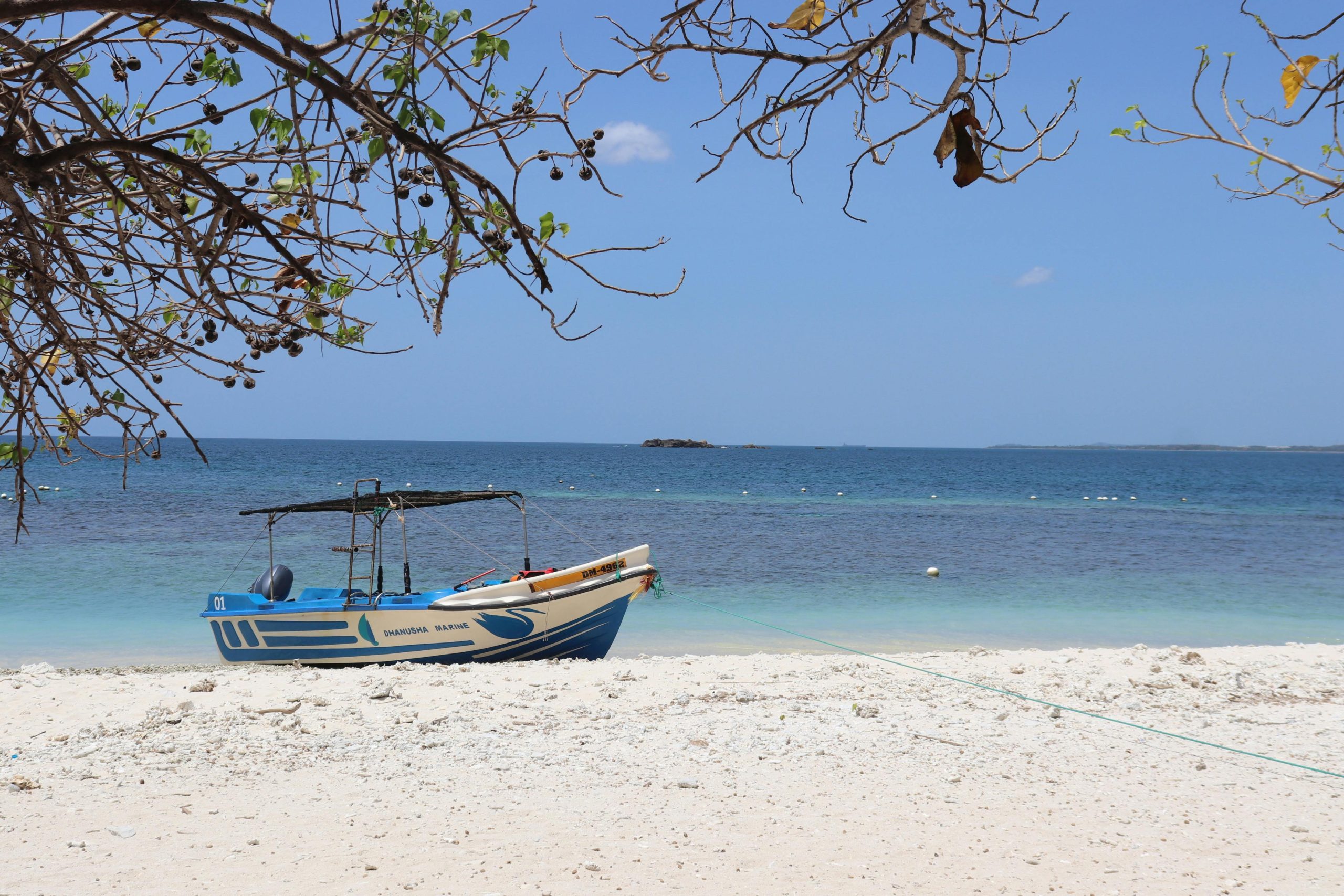 A serene view of a boat on a sandy beach in Sri Lanka, under a clear blue sky.